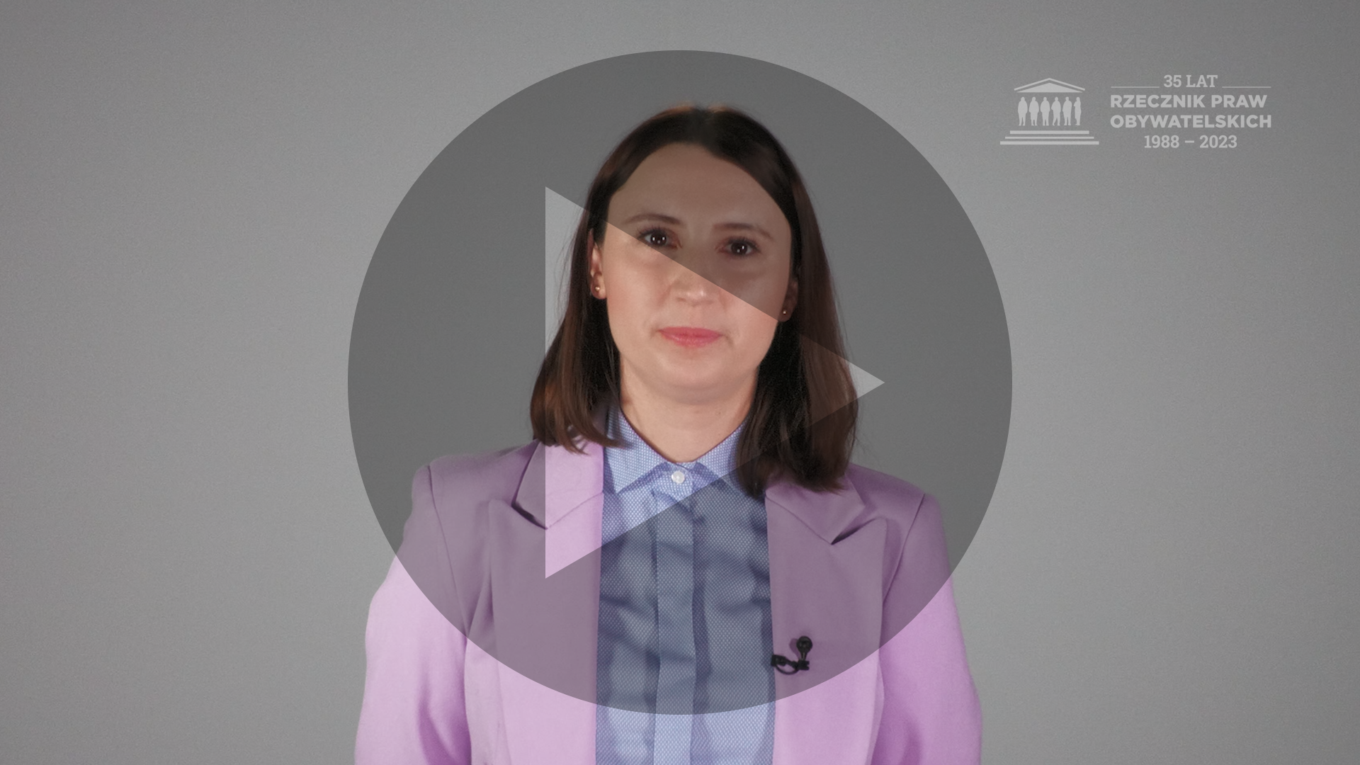 Kadr z nagrania przedstawiający Monikę Wiszyńską Rakowską z naniesionym symbolem odtwarzania wideo - trójkątem w kole
