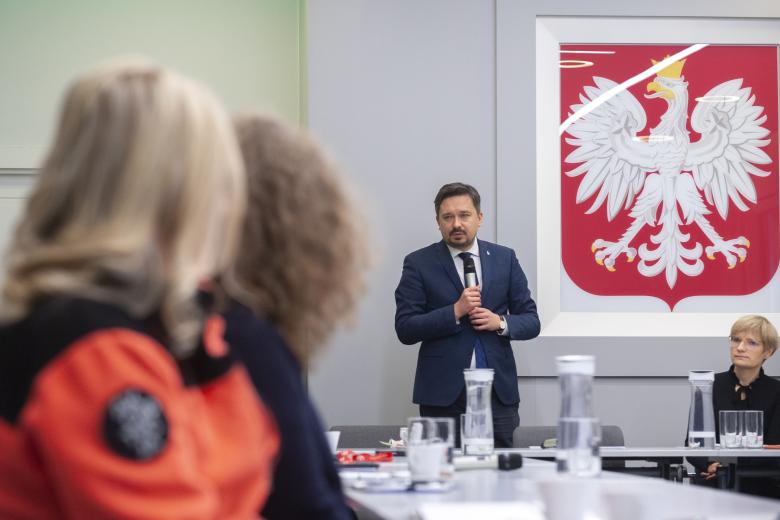 RPO Marcin Wiącek wypowiada się w stronę członków komisji. Na ścianie za RPO znajduje się godło Polski.