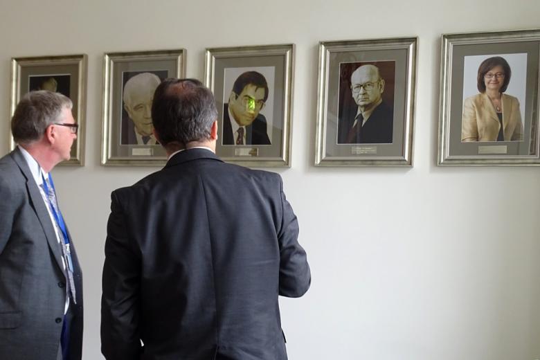 zdjęcie: dwaj mężczyźni stoją tyłem do obiektywu i odladają wiszące przed nimi na ścianie portrety