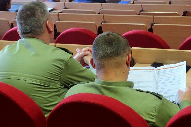 zdjęcie: tyłem widać dwóch mężczyzn w zielonych mundurach, oglądających publikację