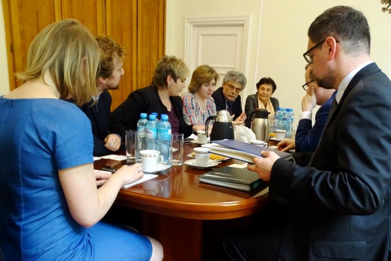 zdjęcie: grupa ludzi siedzi przy owalnym stole, na pierwszym planie kobieta w niebieskiej sukience