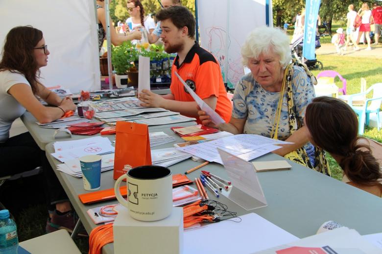 zdjęcie: ratownik w pomarańczowym stroju i starsza pani dyskutują przy stole z dwoma kobietami