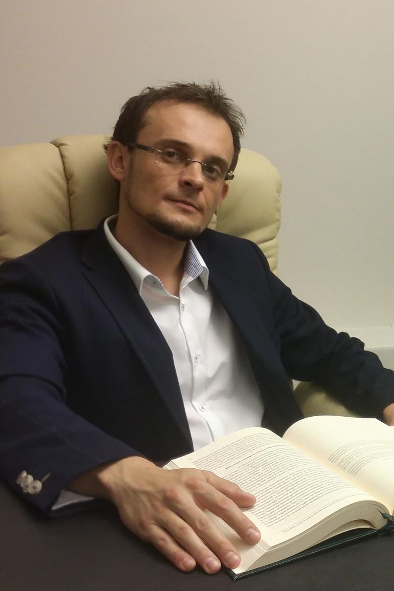 Mężczyzna w garniturze i rozpiętej koszuli siedzi nad książką w fotelu