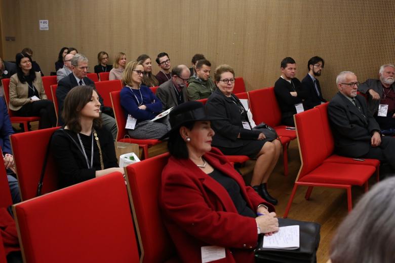 Uczestnicy panelu słuchają dyskusji, czerwone krzesła