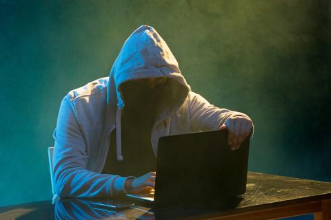 Osoba w kapturze i masce przed komputerem