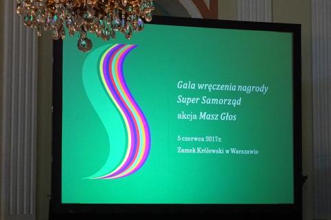 zdjęcie: telebim, na którym na zielonym tle widnieje biały napis: Gala wręczenia Nagrody Super Samorząd akacja Masz Głos