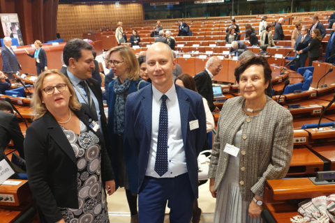 Dwie kobiety i mężczyzna pozują do zdjęcia na tel sali obrad Rady Europy